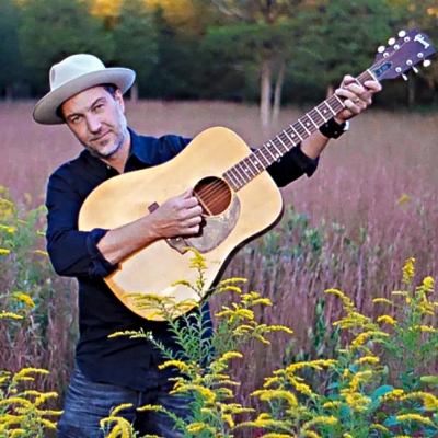 Brian Dolzani with guitar in a field of goldenrod